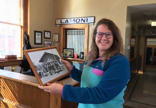 Assistant Professor of Art Karen Gergely at City Hall holding a framed black and white photo of the old filling station in town
