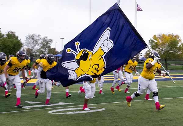 Football team runs on the field waving Yellowjackets flag