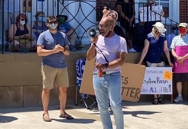 Graceland Seminary Director Zac Harmon-McLaughlin looks on as Darron Story speaks to the crowd of protestors.