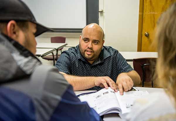 Male professor instructs a male and female student in the classroom