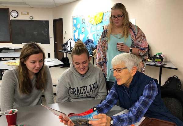 Lorrie Long, RSVP volunteer, reading through a book with two female students