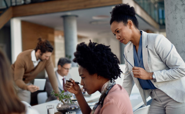 Black female executive manager supervises trainee who is working during internship at corporate company.