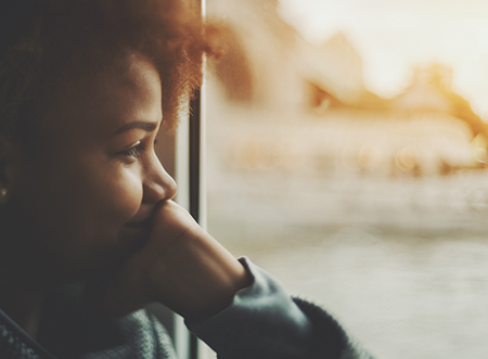 True tilt shift view of smiling black teenager girl near window traveling by ship, biracial young female is laughing and covering her mouth with hand while sitting inside of small cafe near water